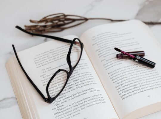 black framed eyeglasses and lipstick on open book