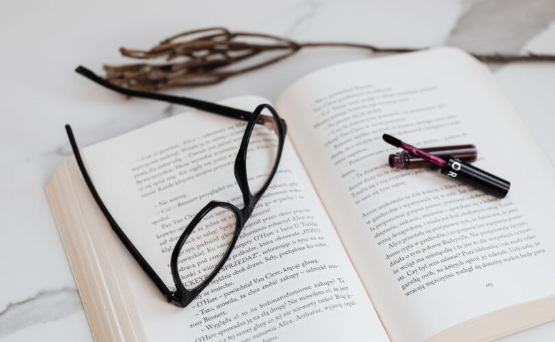 black framed eyeglasses and lipstick on open book